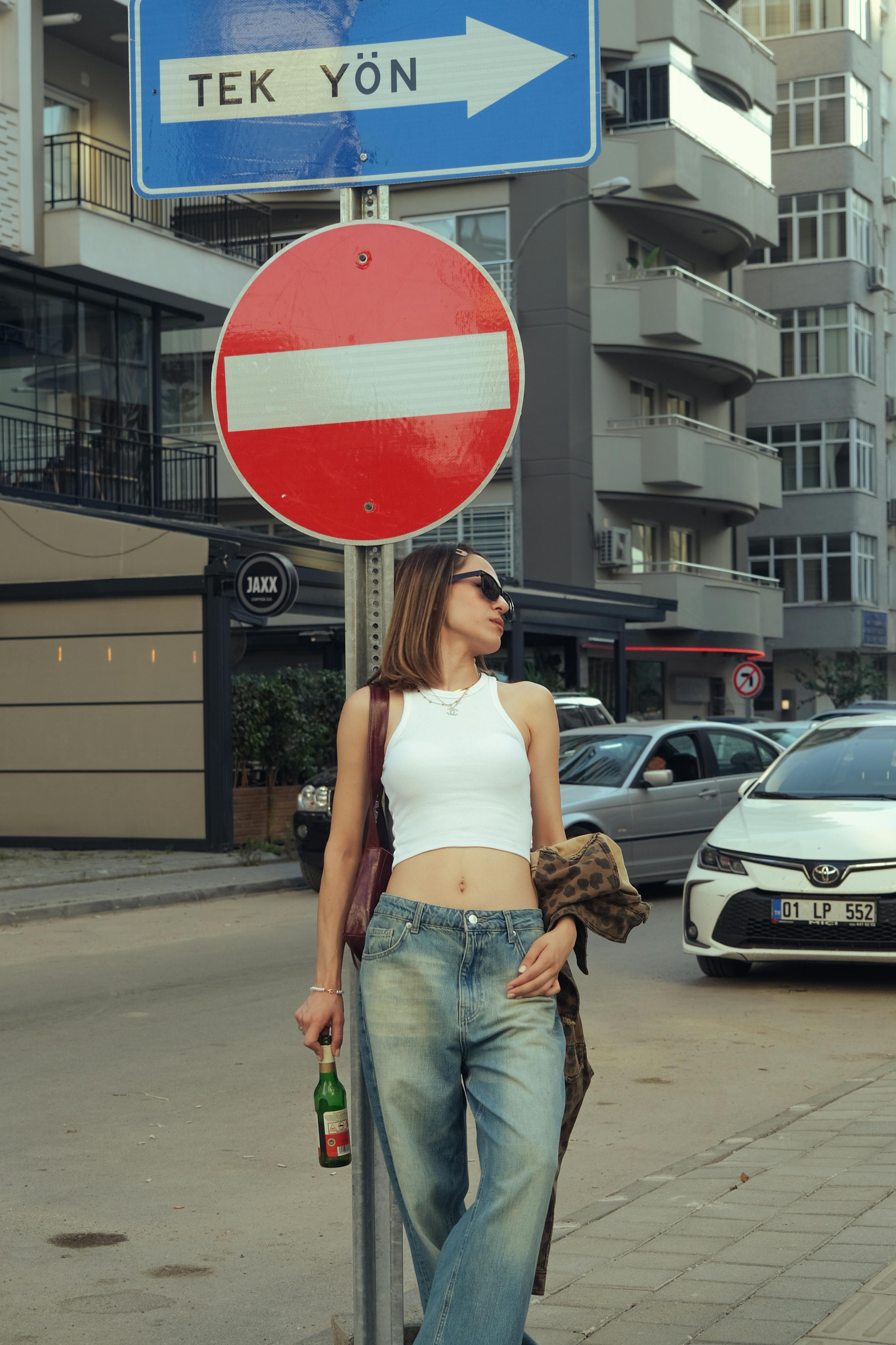 Fashionable woman leaning against a pole in the city, holding a drink, and enjoying a sunny day.
