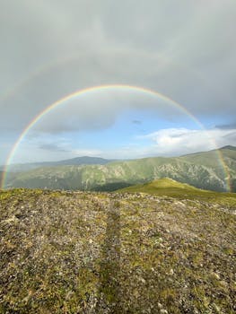Stunning rainbow arches over a scenic mountain range on a bright day.