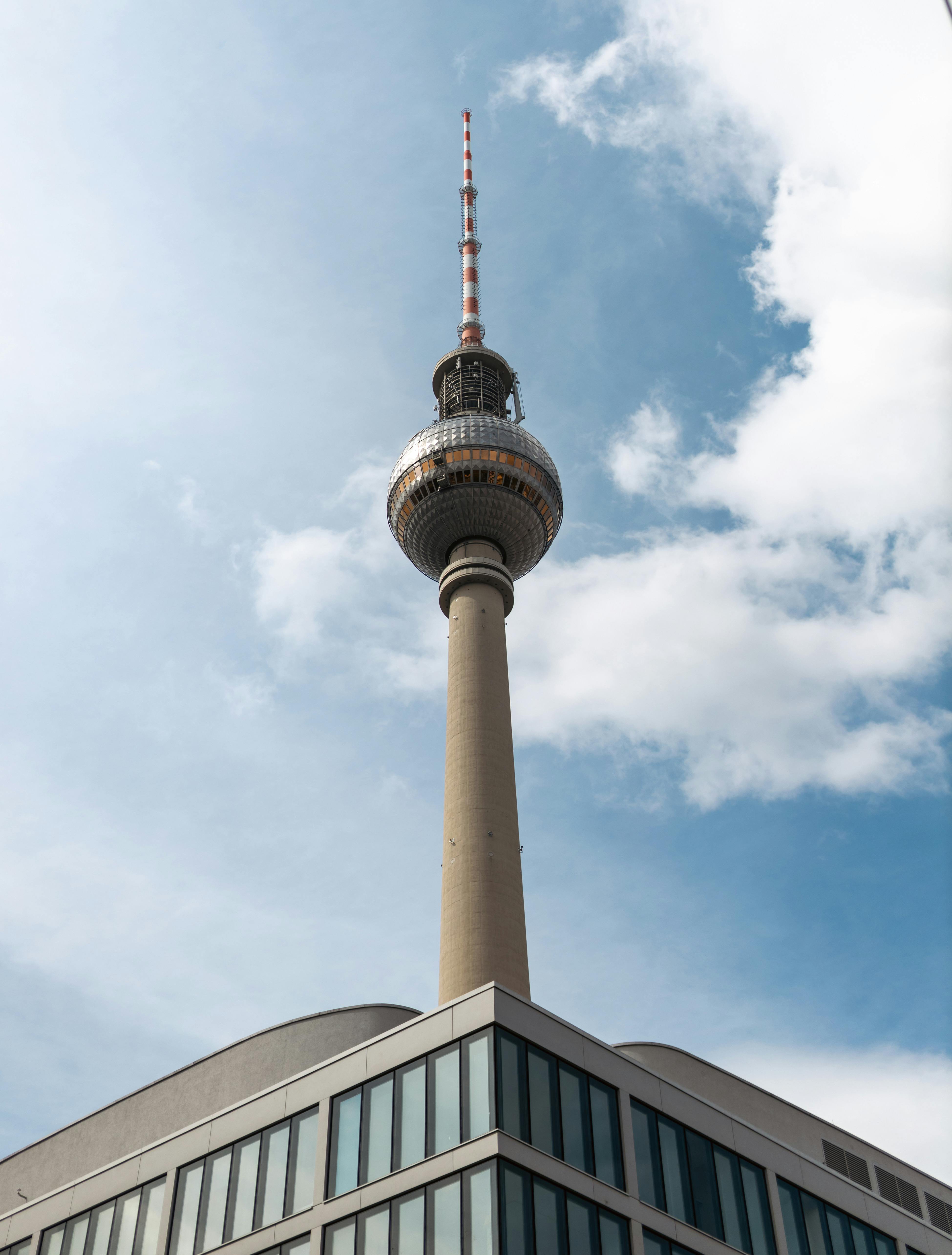 Low angle view of the Berlin TV Tower on a sunny day with clouds in the sky, highlighting urban architecture.