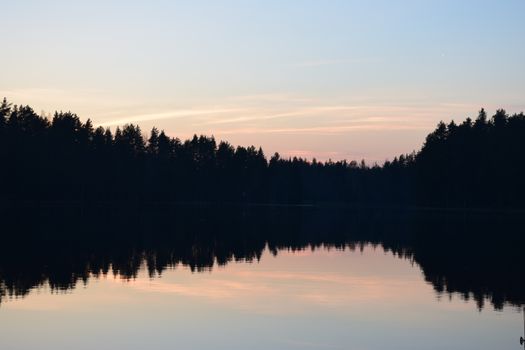 Serene sunset with tree silhouettes reflecting over a calm lake in Võru, Estonia.