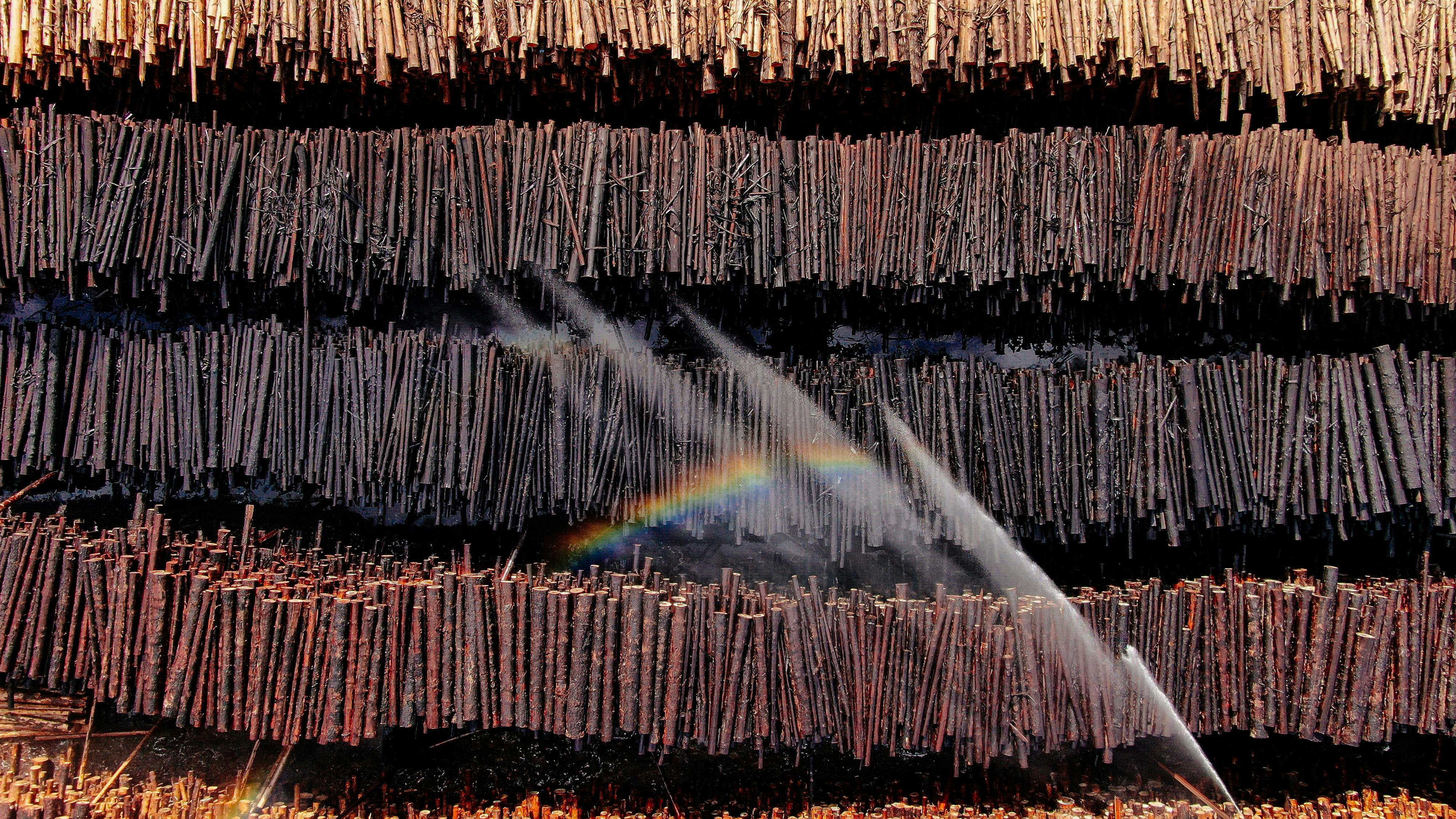 Drone view of stacked wood with sunlight and rainbow effect due to water sprinkling.