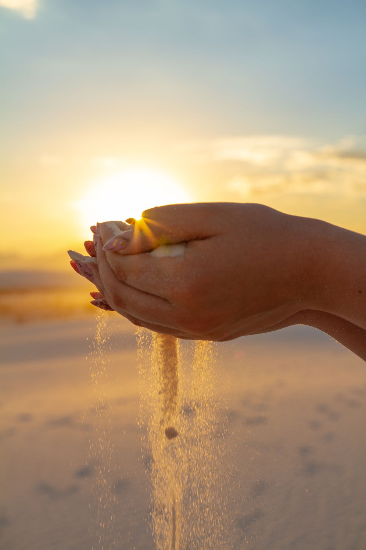 Mains laissant s'écouler du sable au coucher du soleil