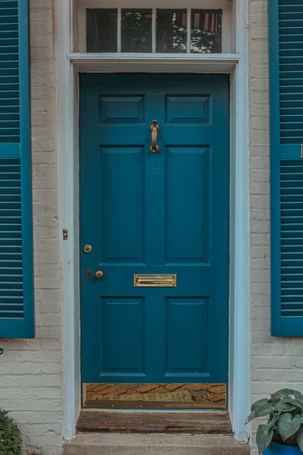 A classic blue door with brass accents and shutters on a brick house exterior.