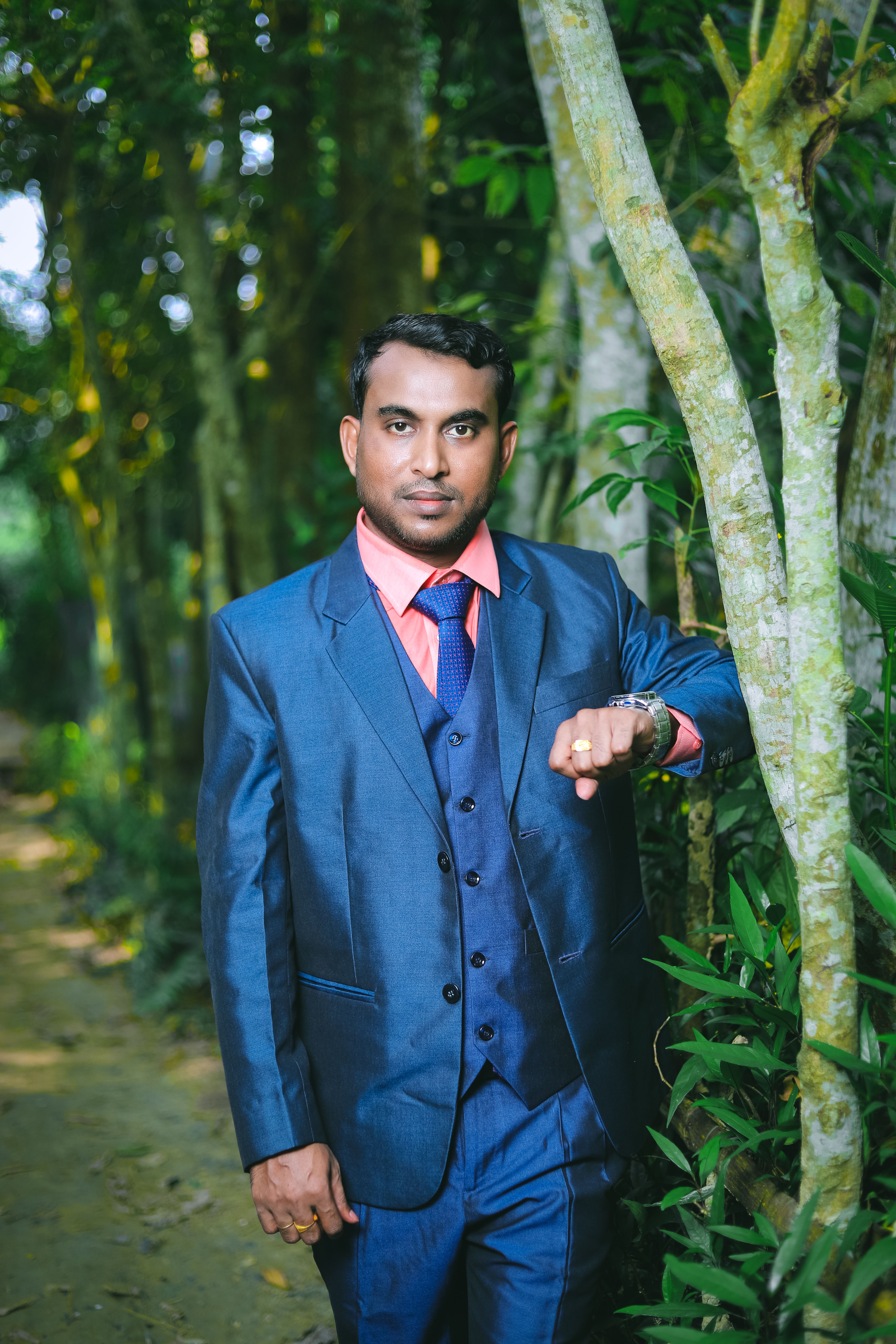 Man in a blue suit standing in a lush forest, showcasing elegance and style.