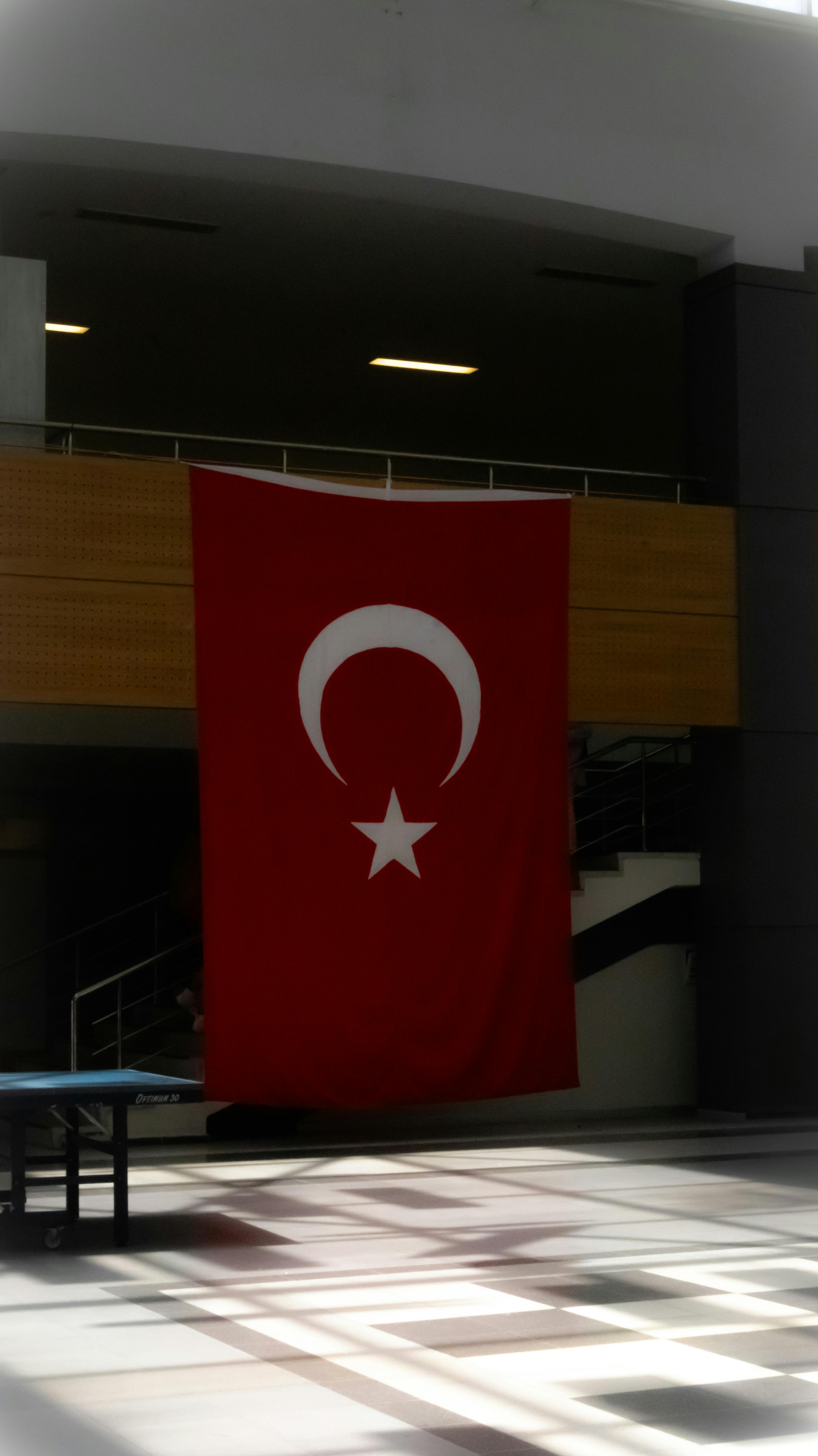 Indoors view of Turkish national flag hanging in a modern hall with natural light.