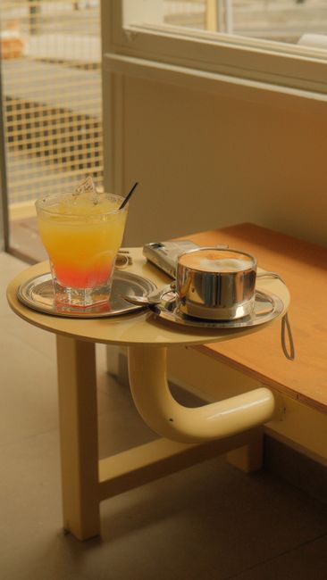 A fresh cocktail and coffee cup on a bench-side table in a warm café ambiance.