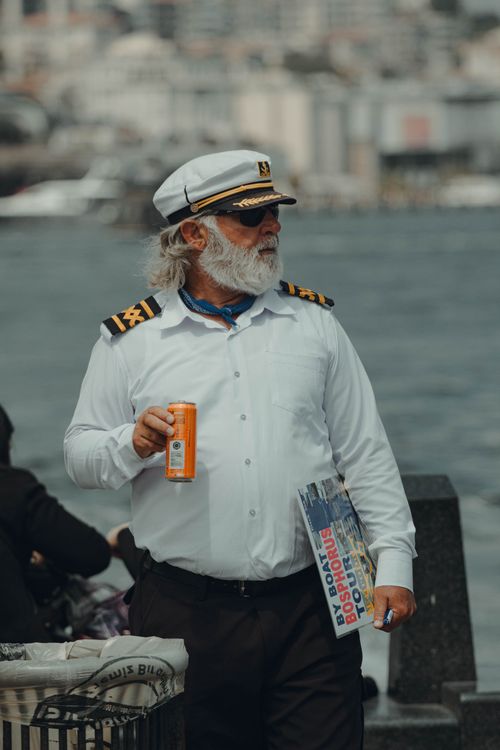 Free Bearded captain holding a drink and newspaper by the Istanbul shore. Stock Photo