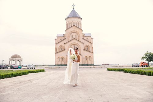Free Beautiful bride in elegant wedding dress standing outside a grand church with a bouquet. Stock Photo