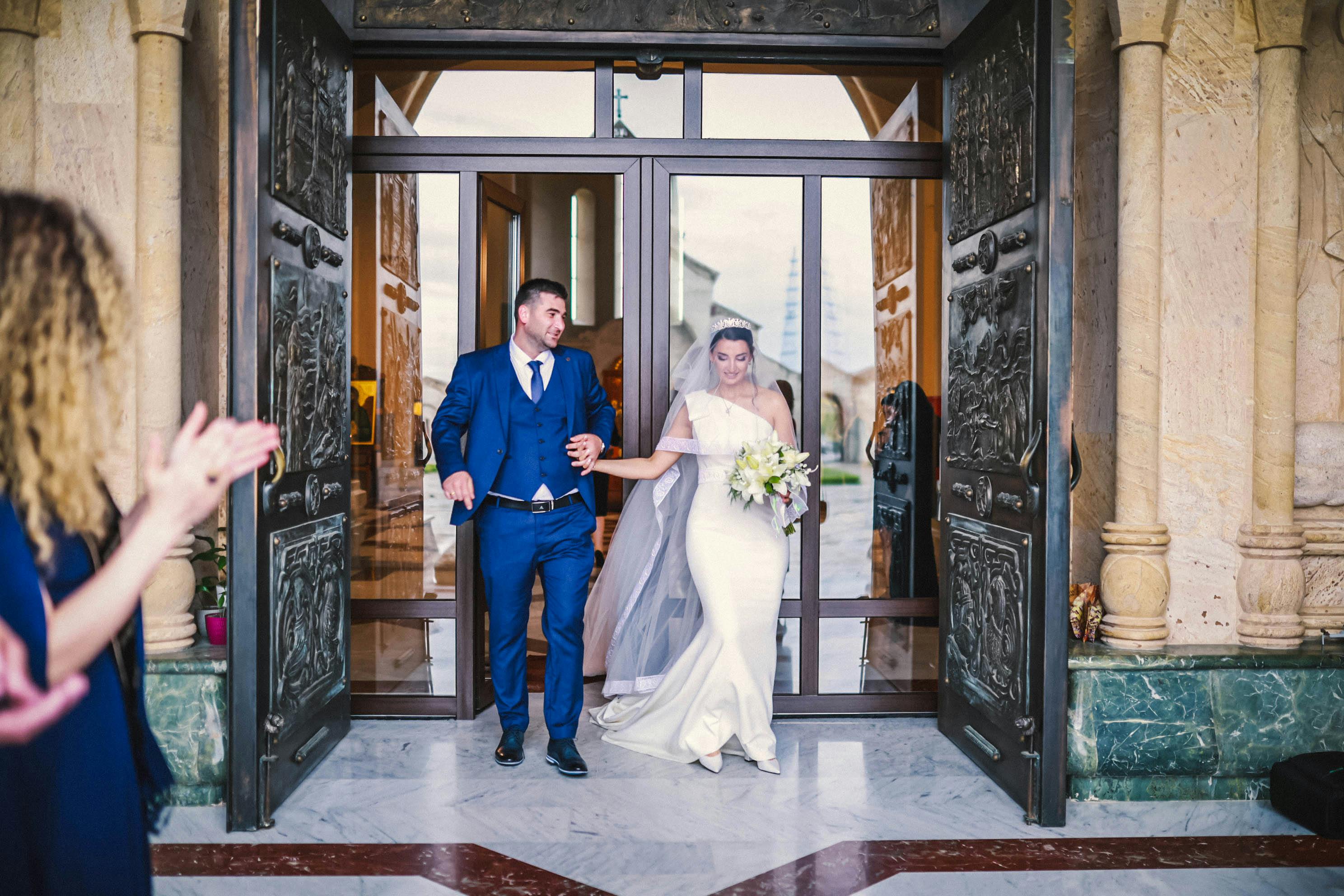 Bride and groom exiting church, hand in hand, celebrating their wedding day with smiles and elegance.