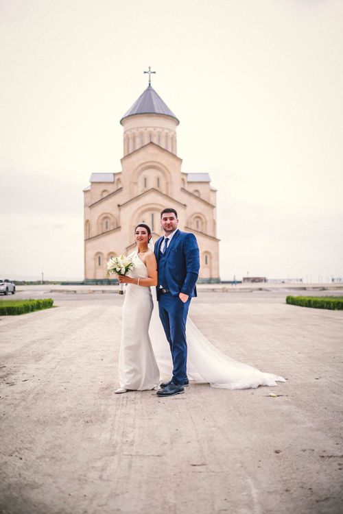 Free Bride and groom pose elegantly in front of a historic church, capturing timeless wedding memories. Stock Photo