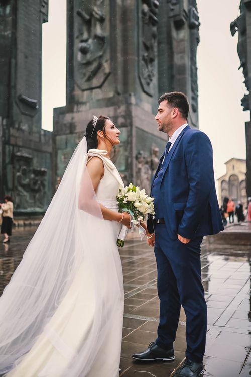 Free Bride and groom in elegant attire sharing a moment at a historic monument. Perfect wedding scene. Stock Photo
