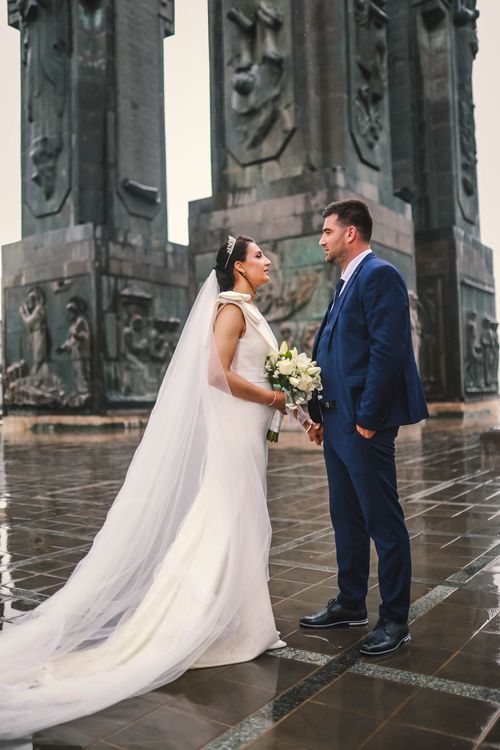 Free Bride and groom in elegant attire at a monumental setting, a perfect wedding moment captured outdoors. Stock Photo