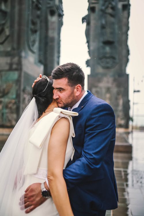 Free A couple shares a romantic embrace in formal attire with majestic stone monuments in the background. Stock Photo