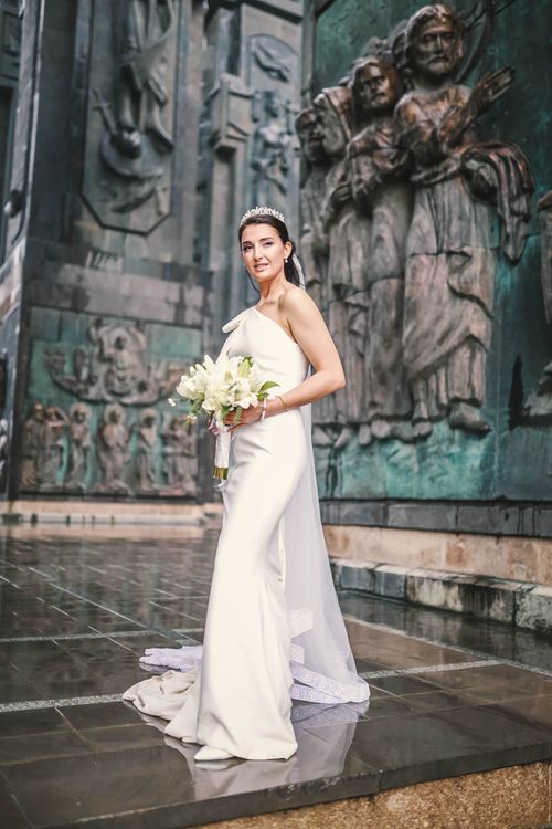 Free Beautiful bride in wedding dress holding bouquet, standing by iconic monument. Stock Photo