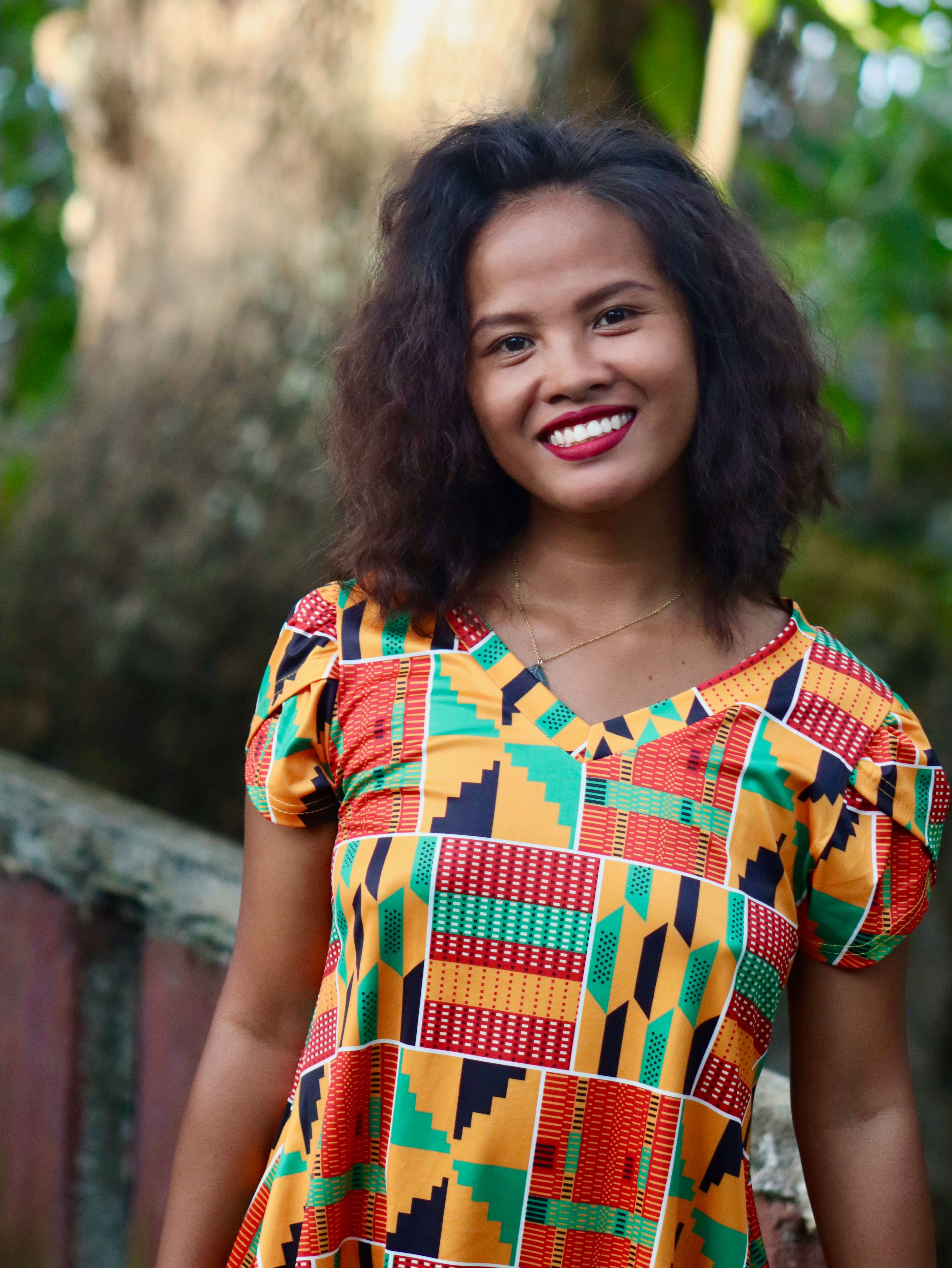 Vibrant portrait of a smiling woman in a colorful patterned dress surrounded by nature.