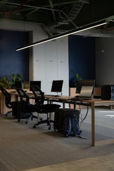 Contemporary coworking office space with desks, chairs, and computers in natural light.