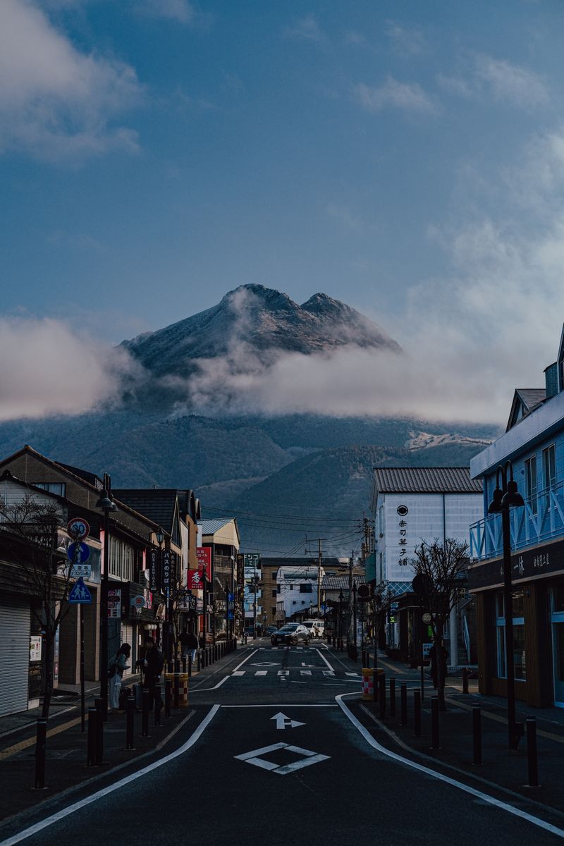 Yufuin town street with Mount Yufu dominating the horizon through morning clouds — the quintessential Yufuin scene