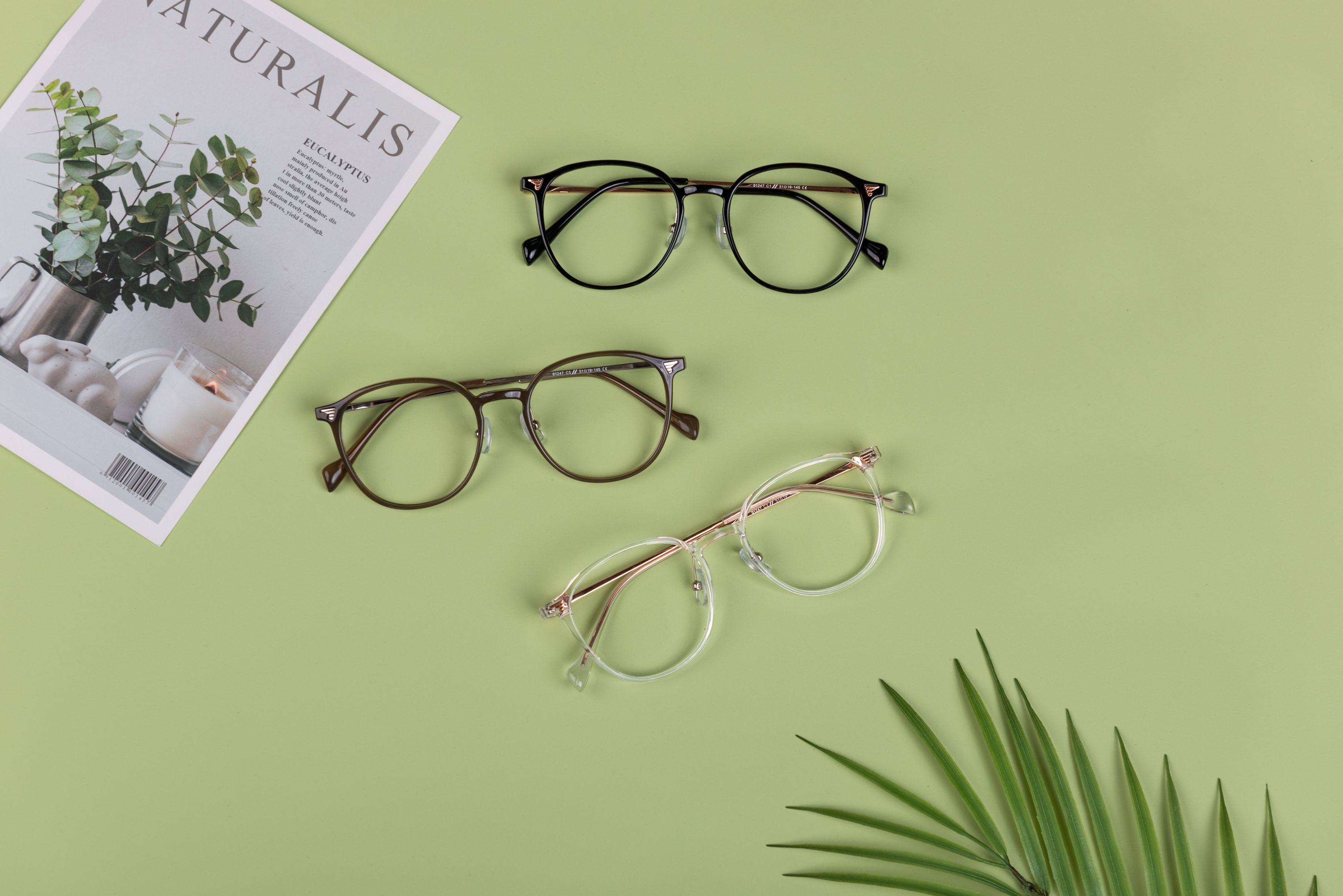 Top view of stylish eyeglasses on a light green background with a magazine, perfect for fashion and design themes.