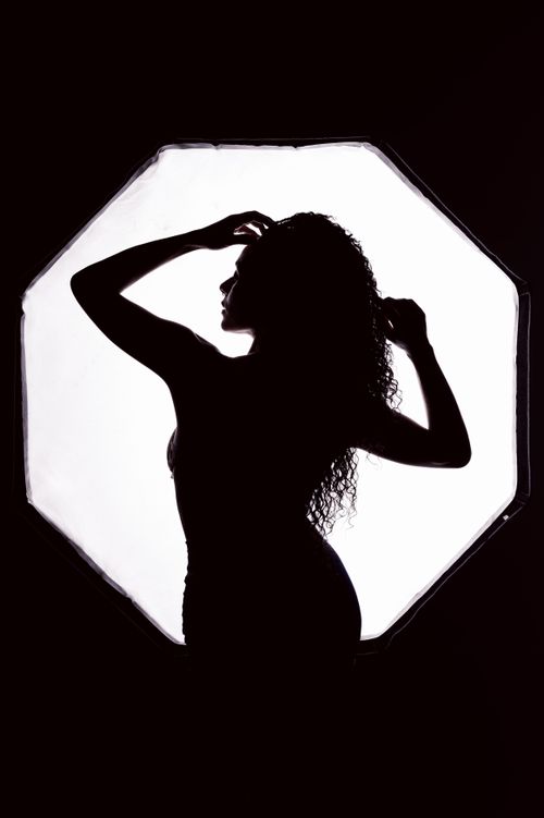 Free Silhouette of a woman posing elegantly in a studio with a luminous softbox backdrop. Stock Photo