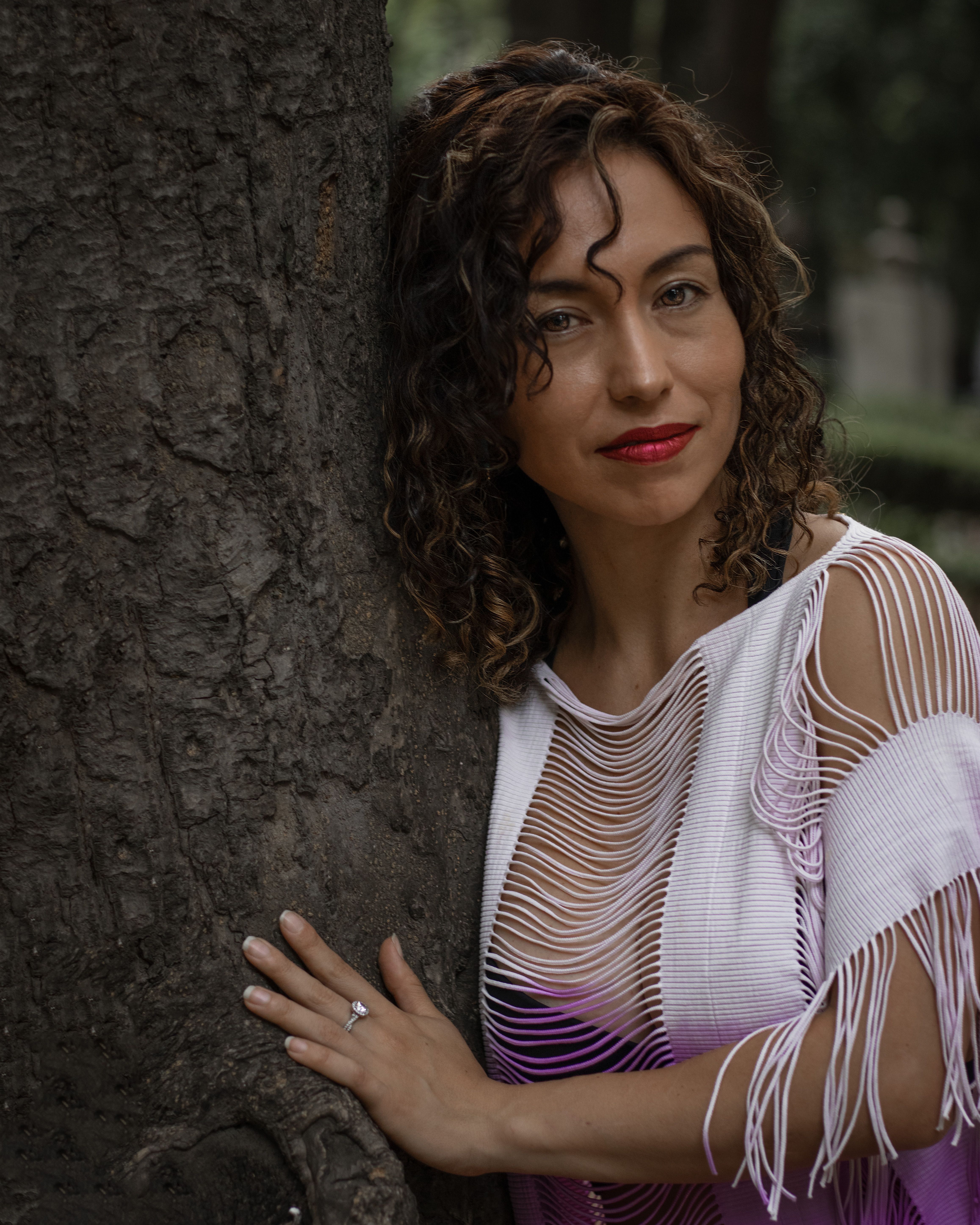 Beautiful woman in a stylish dress poses by a tree in Mexico City.