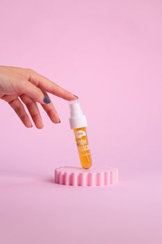 Close-up of a skincare serum in a plastic tube on a pink stand, held by a hand.
