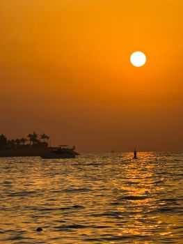 Captivating sunset view over Dubai's coastline with silhouetted palm trees and luxurious yachts.