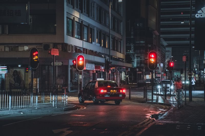 Red taxi waits at a traffic light on city streets of Hong Kong at night, capturing urban life.