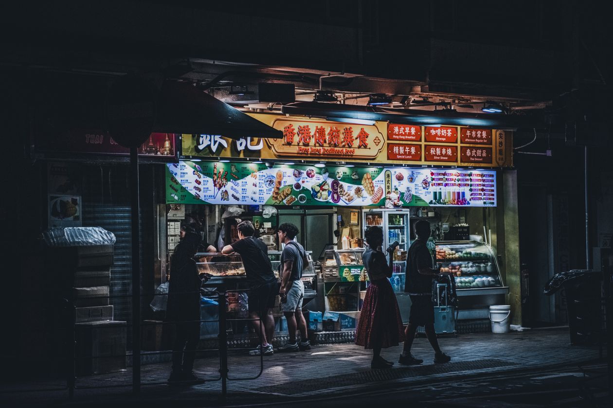 A Hong Kong street food stall illuminated at night with passersby