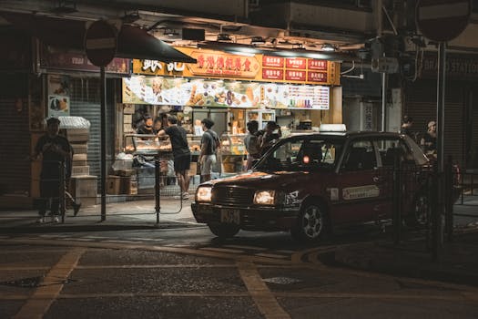Ambient street food stall scene in Hong Kong with a vintage taxi in the foreground during night.