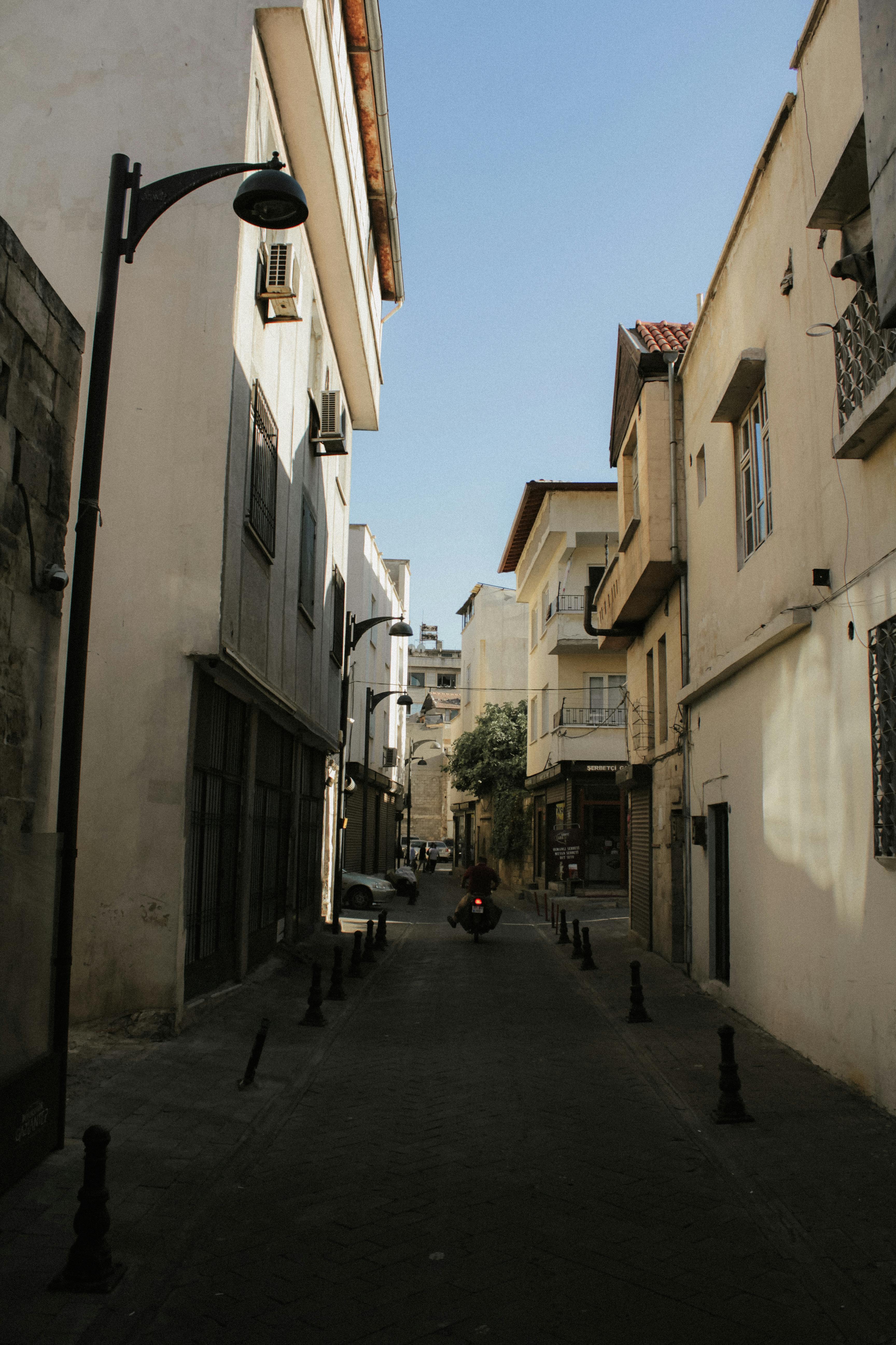 A quiet alleyway in Gaziantep, Türkiye, featuring traditional architecture and a lone motor scooter.