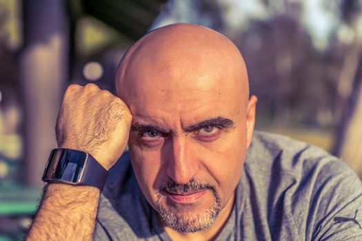 Bald man with smartwatch in an outdoor portrait setting, exuding confidence.