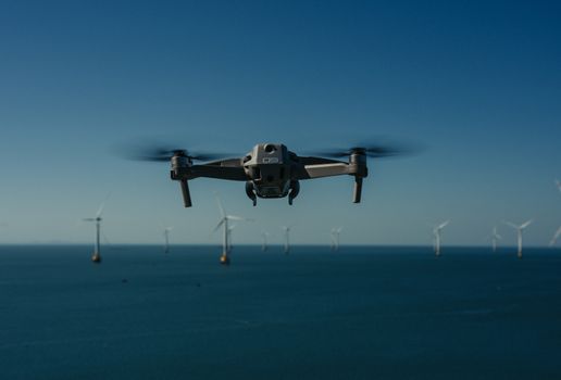Aerial view of a drone flying over the ocean amidst wind turbines.