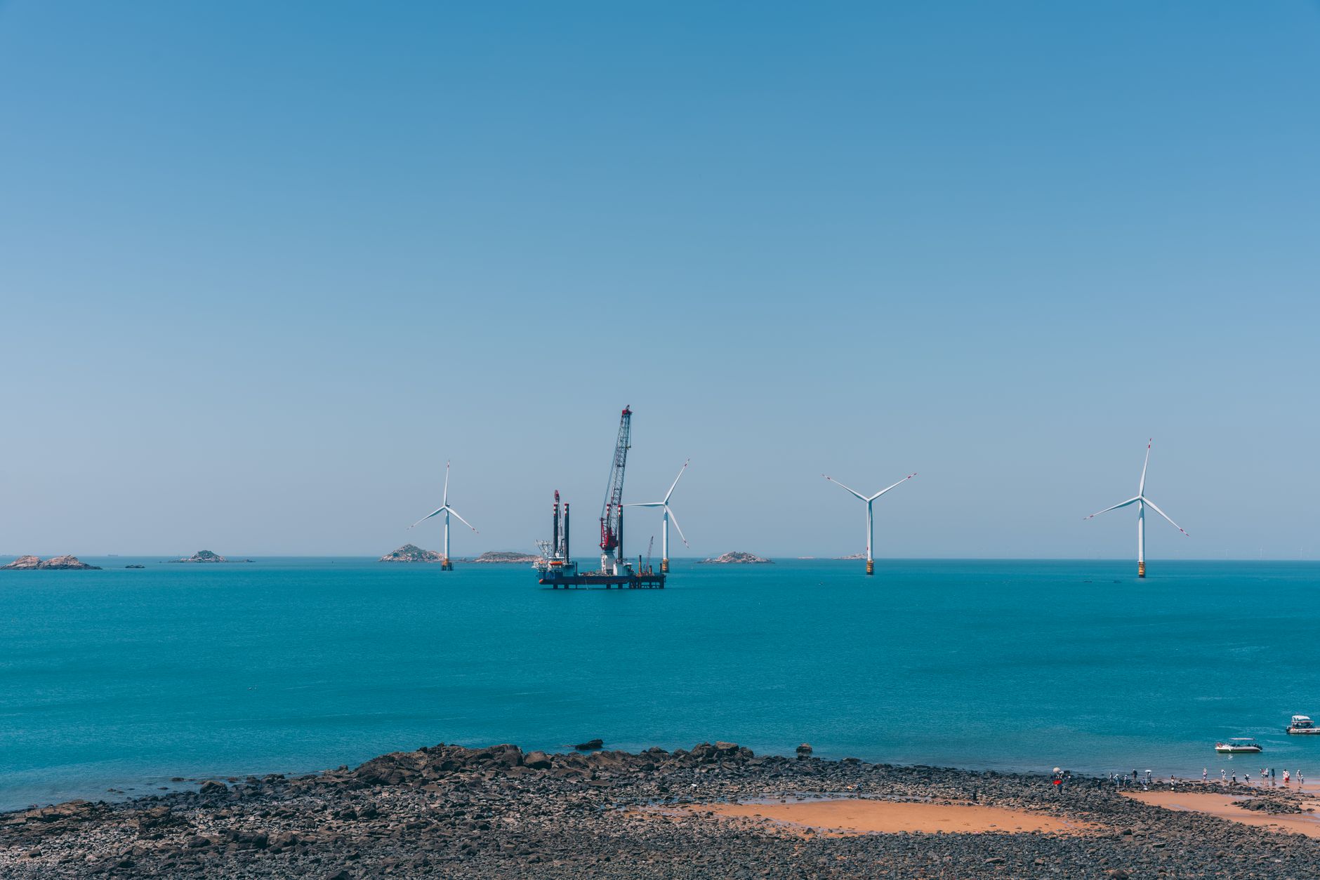 A serene view of offshore wind turbines against a clear blue sky with calm ocean waters.