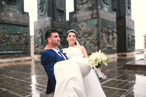 Free Groom carries bride with bouquet outdoors, celebrating wedding. Stock Photo