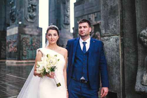 Free A sophisticated couple poses in wedding attire amidst urban sculptures. Stock Photo