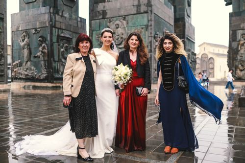 Free A group of elegantly dressed women at an outdoor wedding ceremony with a city backdrop. Stock Photo