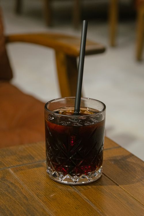 Free A close-up shot of a crystal glass filled with iced cola and a straw, placed on a wooden table indoors. Stock Photo