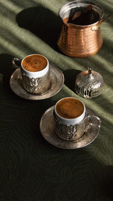 Beautiful silver Turkish coffee cups with intricate designs on a rustic green table.