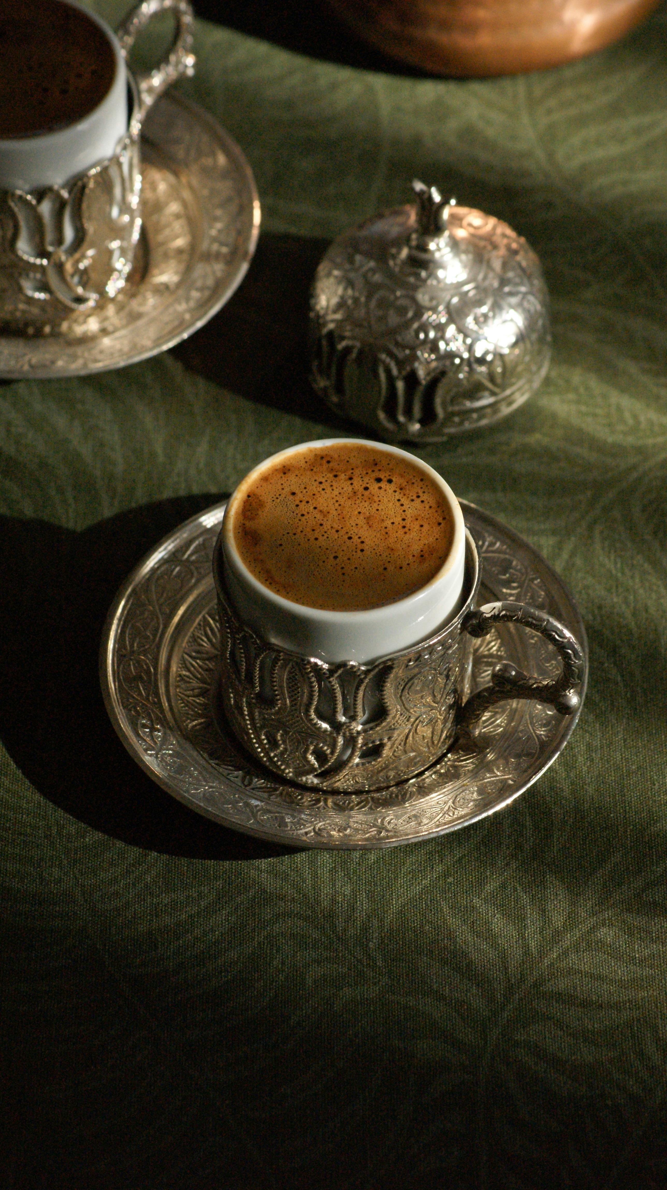 A close-up of a brewed coffee in an ornate silver cup on a green tablecloth.