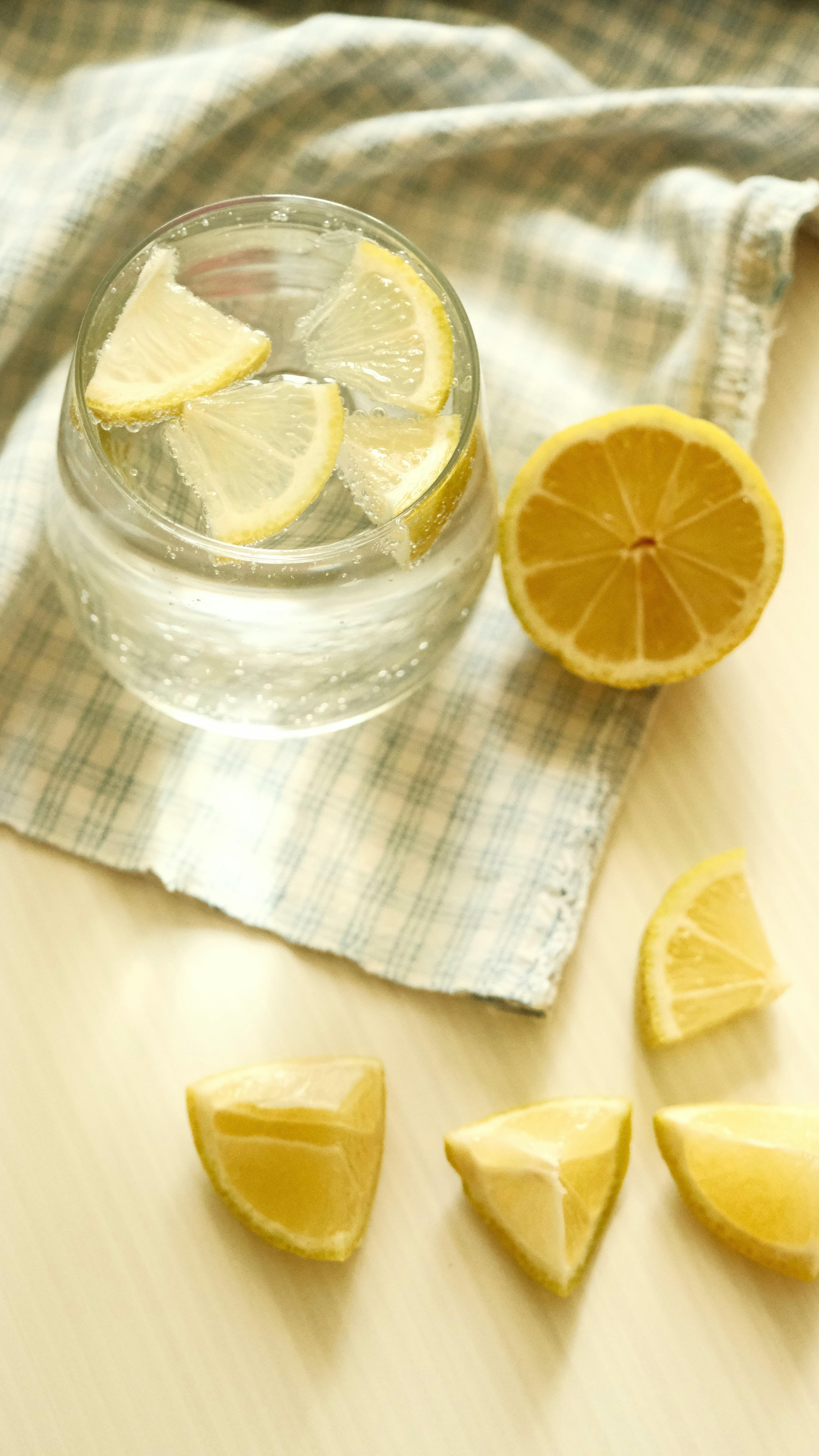 A still life photo of lemon slices in water on a cloth with warm lighting.