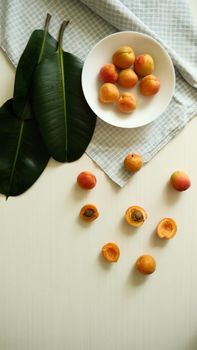 Aesthetic composition of apricots and green leaves on a white checkered tablecloth.