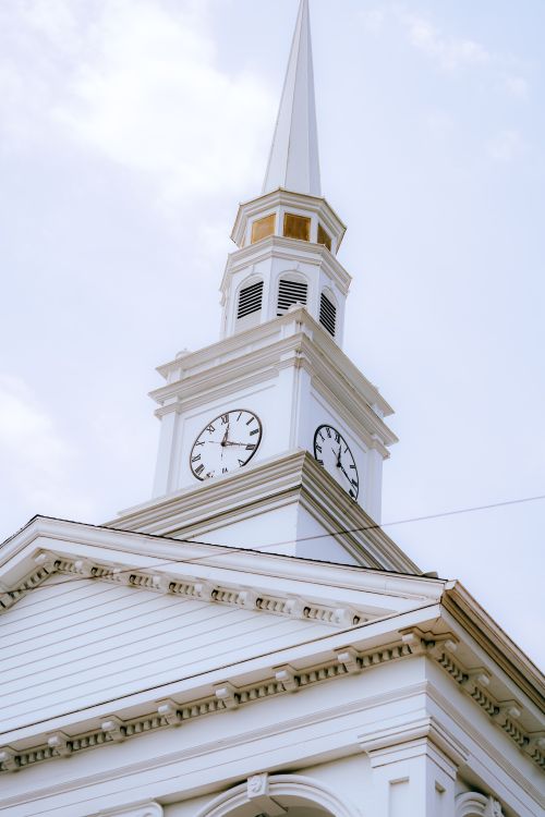Free Close-up of a white church steeple with clock tower against a blue sky backdrop. Stock Photo