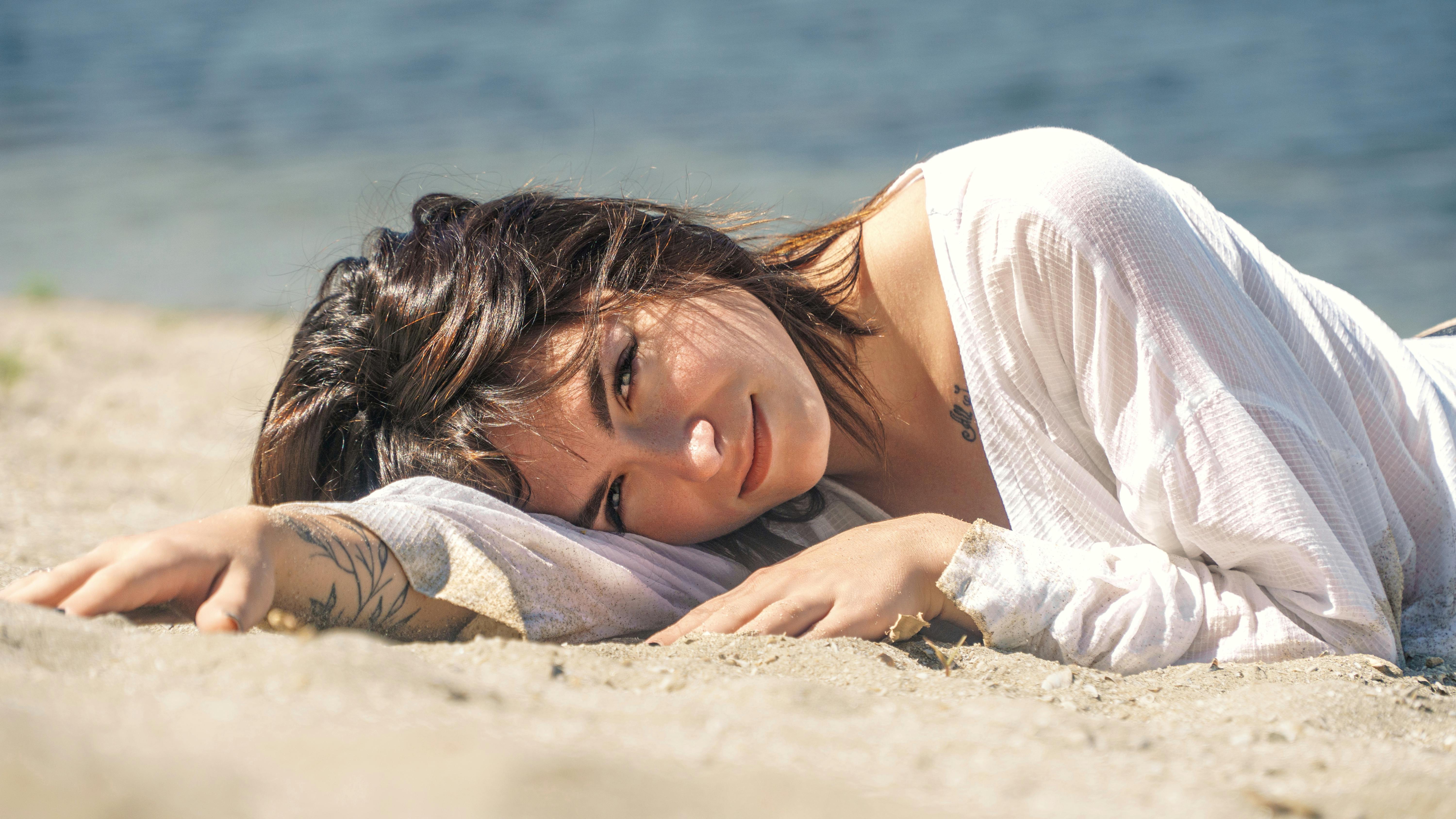 a woman laying on the beach with her head in her hands