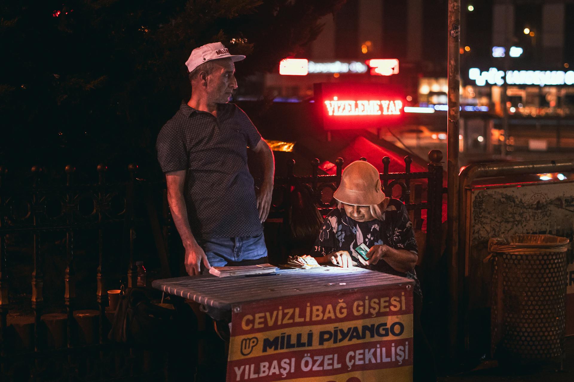 Street vendors selling lottery tickets under neon lights at night in an urban setting.