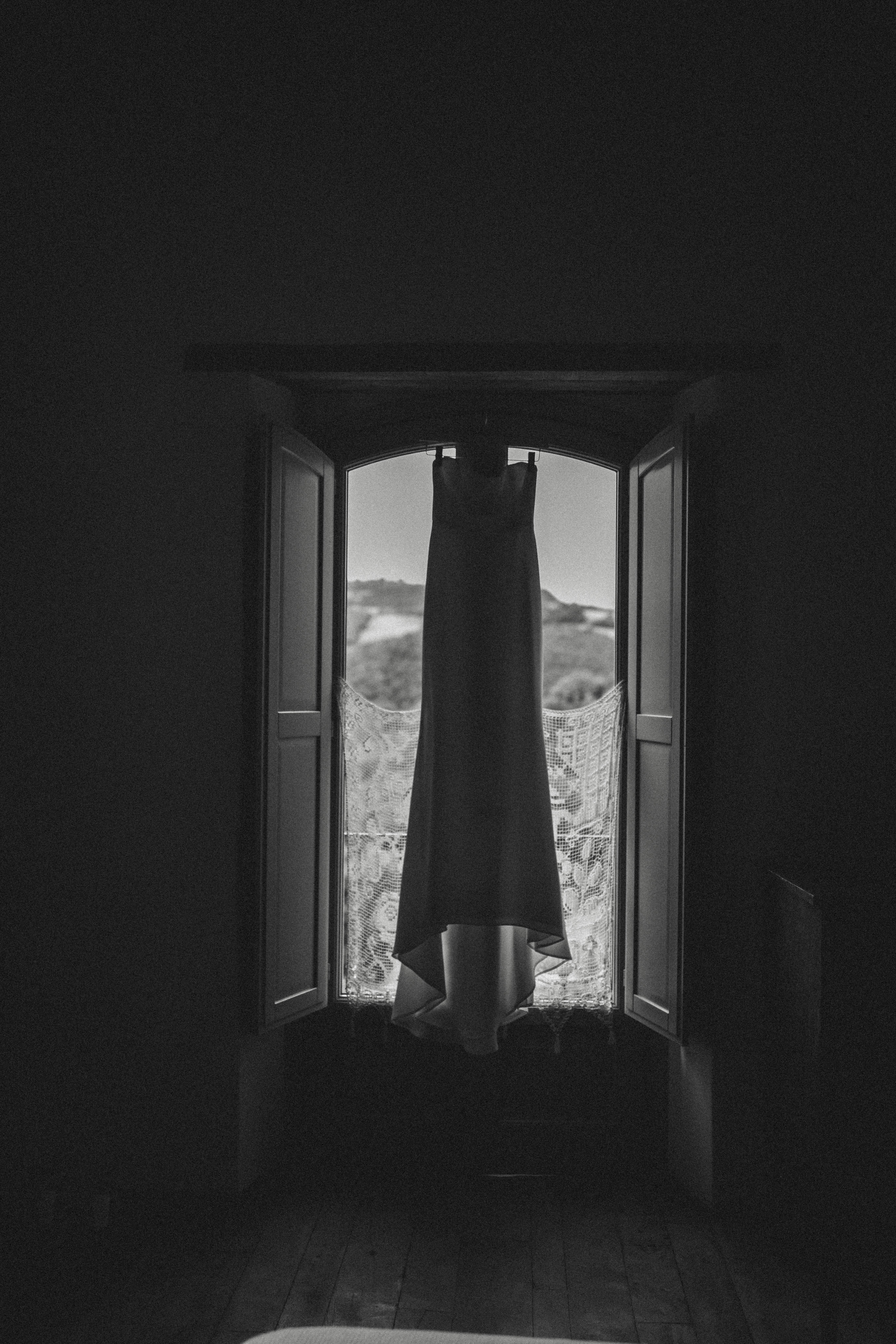 Silhouetted view of an elegant dress hanging in a vintage-style window.