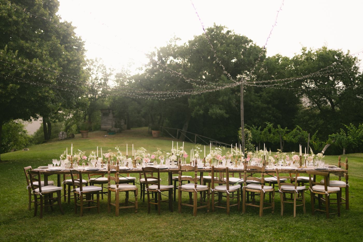 Long garden table dressed in candles and blush florals under fairy lights — representative image