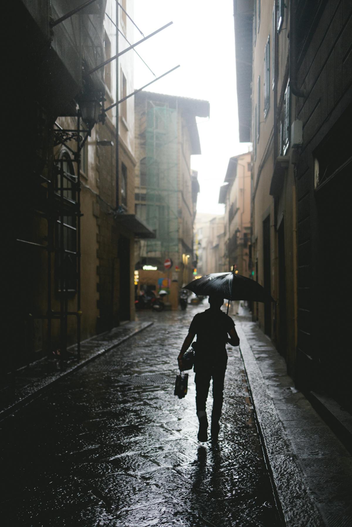 Passante con ombrello che cammina lungo una via bagnata del centro storico di Firenze