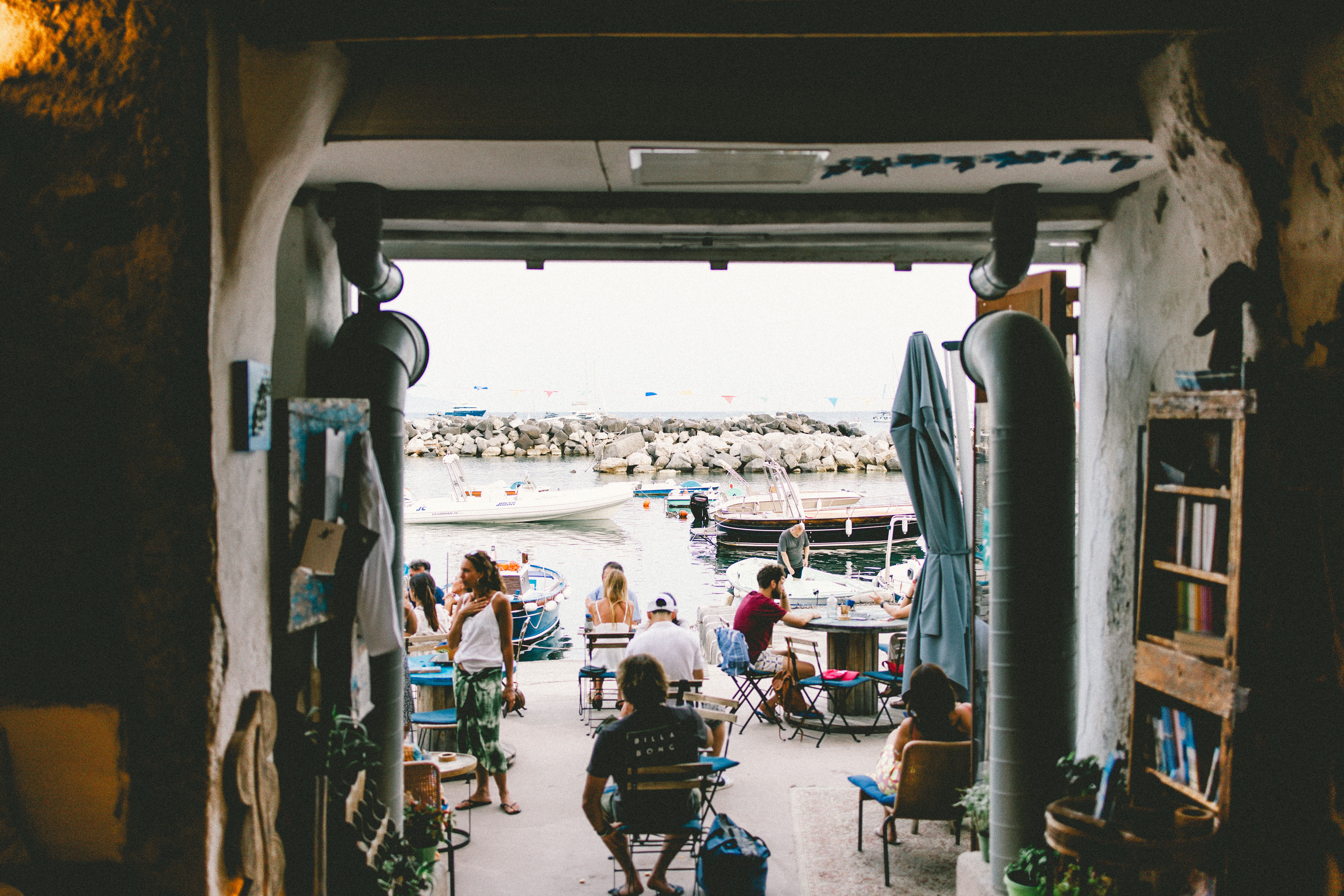 Cozy marina cafe scene with people enjoying a seaside view, boats in background.
