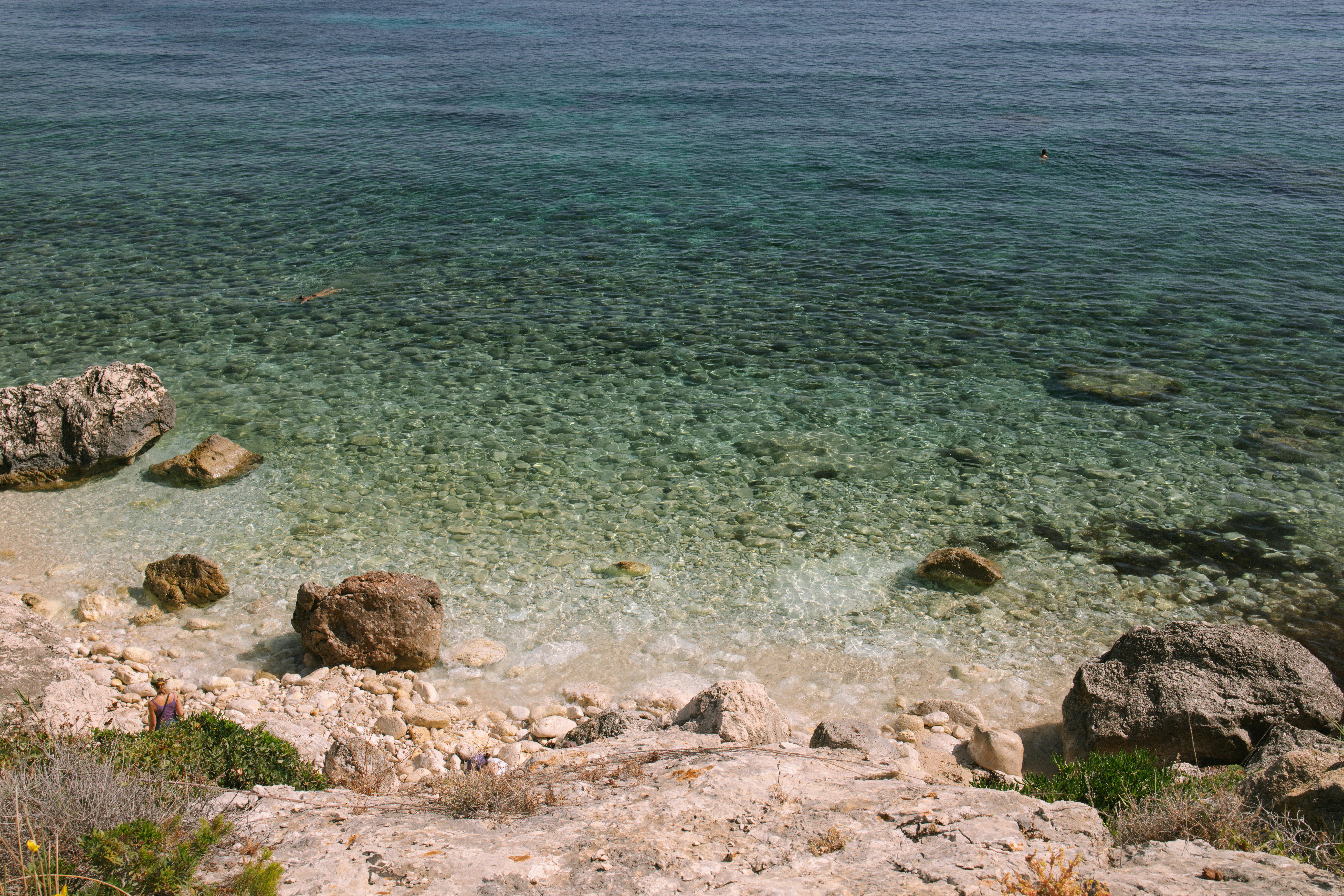 A tranquil rocky beach with clear turquoise waters under the summer sun, perfect for travel and relaxation. - Photo by Josh Withers on Pexels