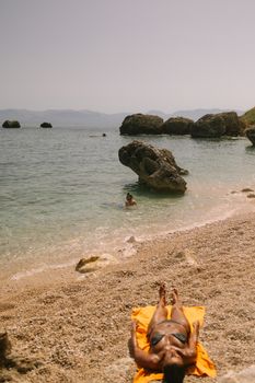 Woman sunbathing on a rocky beach by the sea, enjoying a peaceful summer day.
